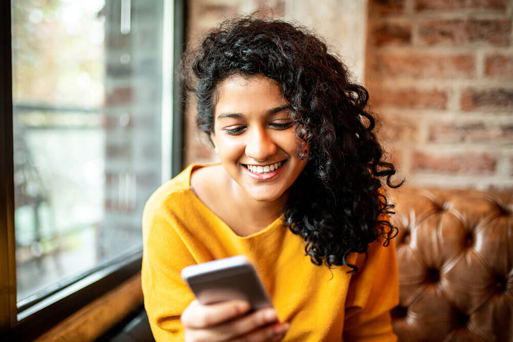 Indian woman smiling watching Lottoland Presents Jeetenge Hum on her phone