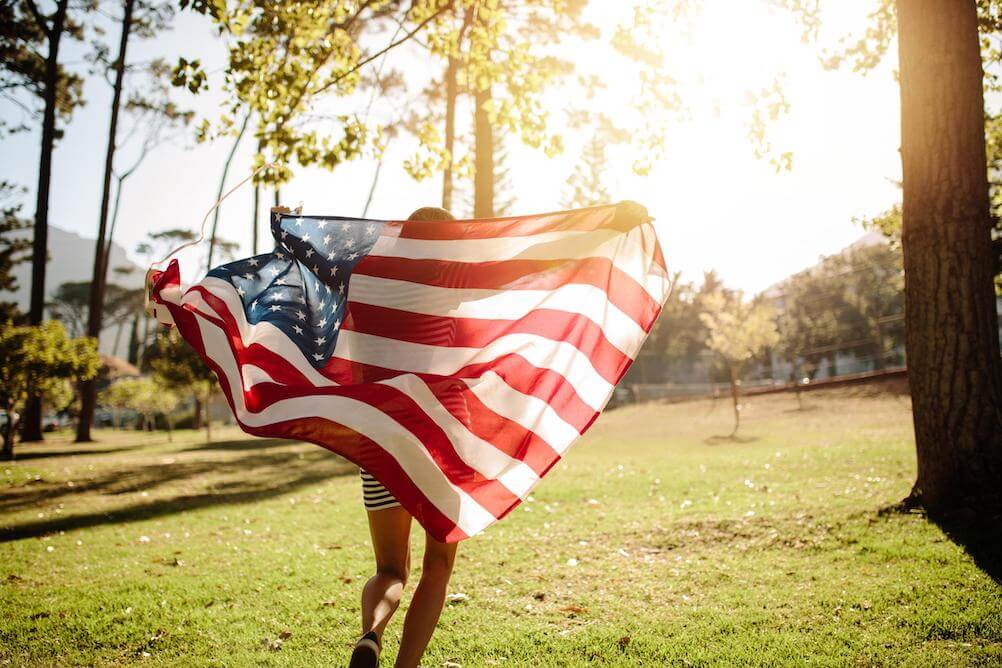 Powerball-Jackpot woman-celebrating-with-american-flag-through-sunny-park