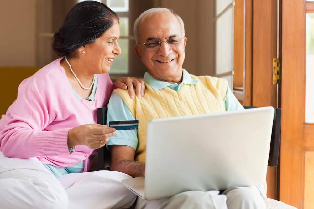 Elderly couple smiling at laptop claiming lottery winnings